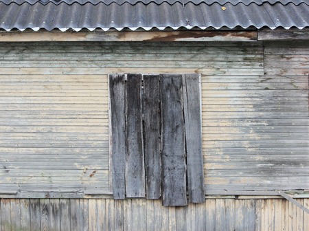 the wall of the wooden house with the old beige paint and boarded up window and slate roofの写真素材