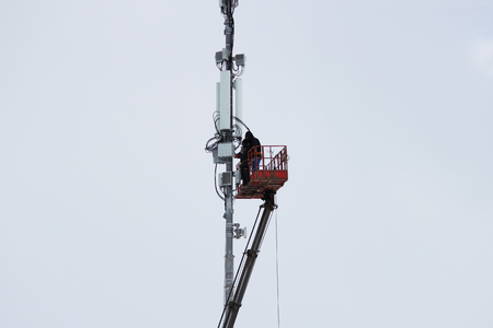 Two workers assemble equipment for telecommunications on the tower with the help of the lift in the winter.の写真素材
