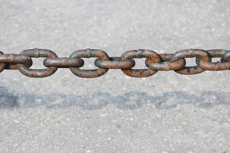 rusty metal chain hanging over the asphalt and casts a shadow.の写真素材