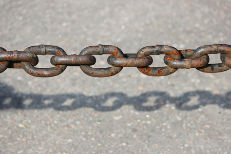 rusty metal chain hanging over the asphalt and casts a shadow.の写真素材