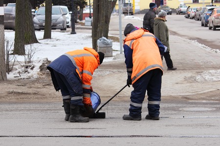 Two road workers in overalls are poured with hot tar on the edge of the road strip when repairing the roadの写真素材