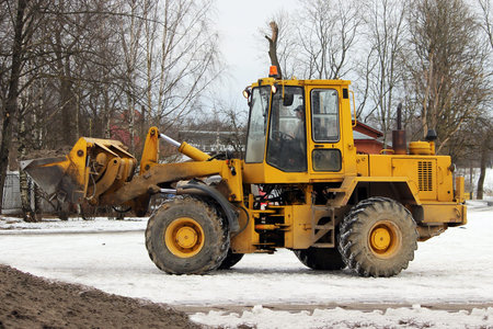 Excavator cleans the road in the city of dirty snow