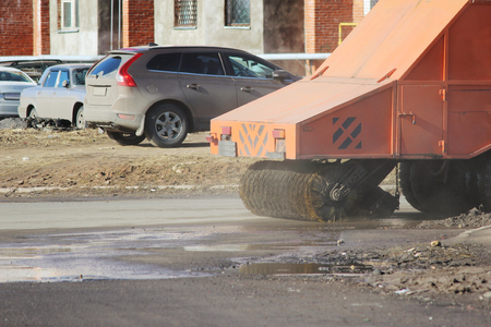 Orange urban sweeper cleans road from dirt with a round brush in the springの写真素材