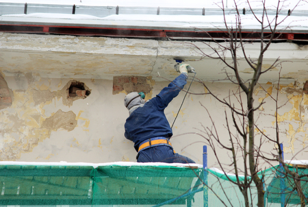 The worker in protective glasses and a respirator processes the wall with an angle grinder before restoration and plasteringの写真素材