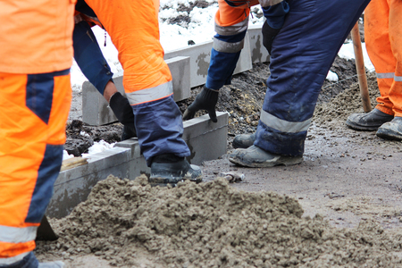 Working stonemasons repair the sidewalk, install curbs before asphalting for roadの写真素材