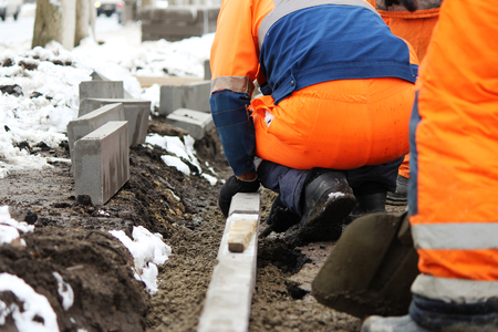 Working stonemasons repair the sidewalk, install curbs before asphalting for roadの写真素材