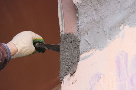 Construction worker wearing worker overall with wall plastering tools renovating apartment house. Plasterer renovating outdoor walls of old house. Construction finishing works.の写真素材