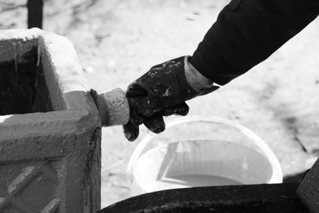 Black and white photo Woman painter paints Concrete base for dirt trash can in grey paint with...