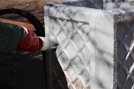 Woman painter paints Concrete base for dirt trash can in grey paint with brush.の写真素材