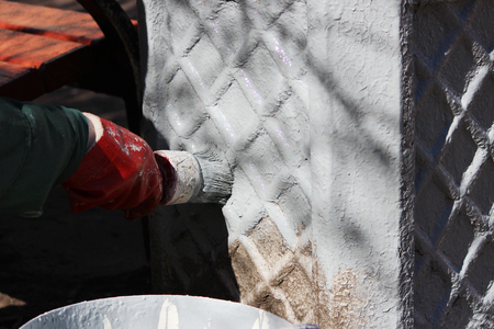 Woman painter paints Concrete base for dirt trash can in grey paint with brush.の写真素材