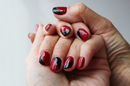 beauty delicate red black manicure with gel varnish on a white wall backgroundの写真素材