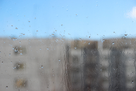 Raindrops on glass and blurred blue sky and house.の写真素材