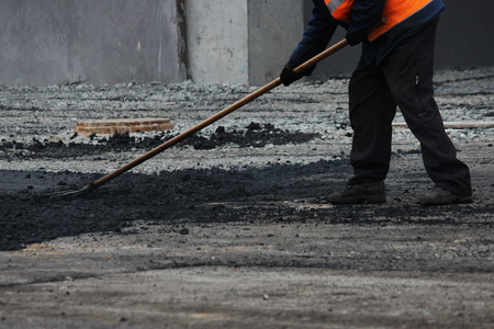 The worker is leveling the crumb of asphalt in the pit with a drag-roller before the paving with a road mini building rollerの写真素材