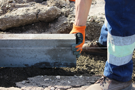 Repair of the sidewalk. Professional working masons in overalls lay curbs before laying stone paving slabs.の写真素材