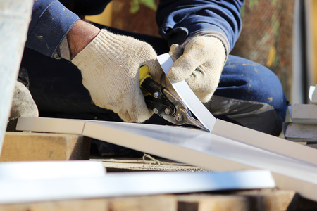 The worker makes the sladding of windows in the restored building in the city, cuts the metal sheet for the slope with scissorsの写真素材