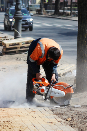 A working mason cuts the sidewalk tile with a circular saw while repairing the sidewalk in the cityの写真素材
