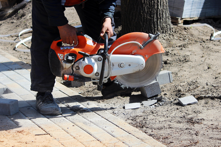 A working mason cuts the sidewalk tile with a circular saw while repairing the sidewalk in the cityの写真素材