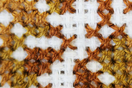 Macro shot fragment embroidery pattern brown thread handmade embroidery, pattern in cross-stitch style on white fabric.の写真素材