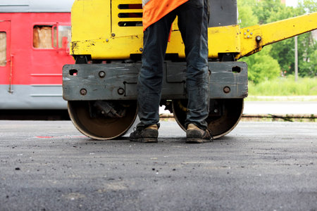 A small compactor covers with asphalt to platform at the railway station. The auxiliary worker...