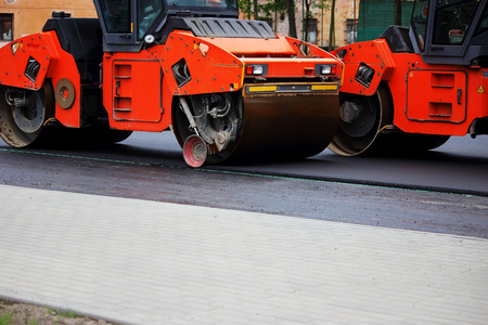 Two heavy compactor tires the upper layer of asphalt in the construction of a parking lot for tourist buses.の写真素材