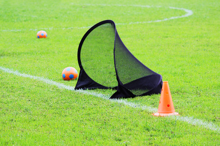 Small football gate for training kids to sports football, balls and plastic limiter in a stadium with green lawn grass.の写真素材