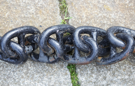 A black metal chain with large links lies on concrete slabs on the ground.の写真素材