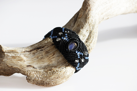 wooden curve stick and a black bracelet on the hand of waxed thread, plastic beads and moonstone in the technique of macrameの写真素材