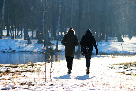 Two people walk together in Park in winter against sunlightの写真素材