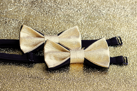 Two festive golden with a black bow tie on a gold backgroundの写真素材