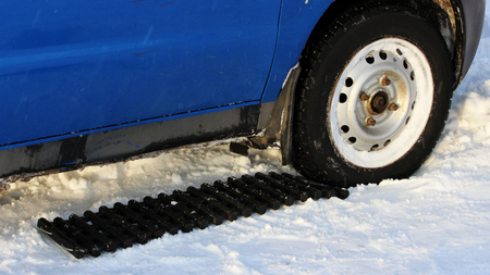 black anti-slip mat of a rectangular shape is placed under the wheel of a low-leveled car after it is stuck in a snowdrift and slips. reportage shootingの写真素材