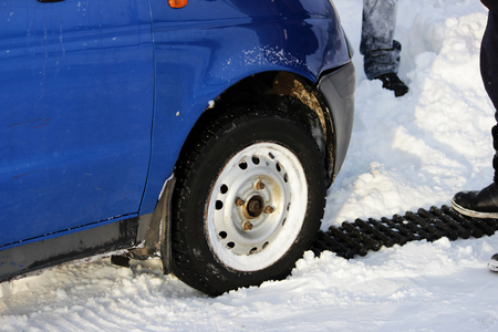 black anti-slip mat of a rectangular shape is placed under the wheel of a low-leveled car after it is stuck in a snowdrift and slips.の写真素材