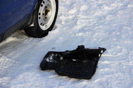 The adjustable jack on the rug on the snow. a blue low-lying car got stuck in a snowdrift. reportage shooting.の写真素材