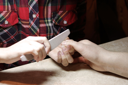 A student at the training courses of a manicure gives shape to nails the hand of a man client with a saw of a buffの写真素材