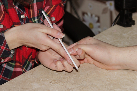 A student at the training courses of a manicure gives shape to nails the hand of a man client with a saw of a buffの写真素材