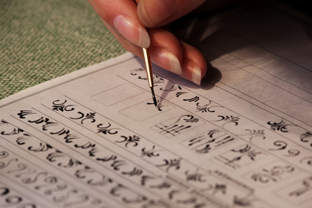 Girl student learns to draw monograms for drawing them on the nails when creating a manicure with lacquer shellac. acrylic black paint, training sheet, fine synthetic brush. reportage shotting.の写真素材