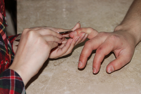 A student at the training courses of a manicure gives shape to nails the hand of a man client with a for removing superfluous cuticles and pterygium.の写真素材
