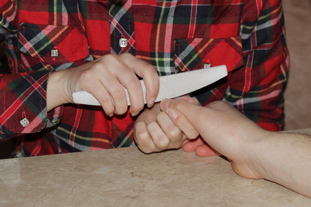 A student at the training courses of a manicure gives shape to nails the hand of a man client with a saw of a buffの写真素材