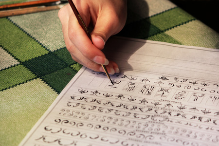 Girl student learns to draw monograms for drawing them on the nails when creating a manicure with lacquer shellac. acrylic black paint, training sheet, fine synthetic brush. reportage shotting.の写真素材