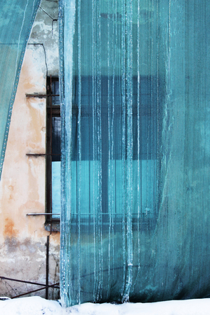 Restoration of the building and a protective green building mesh with frozen water that drained from the roof. Old windowの写真素材