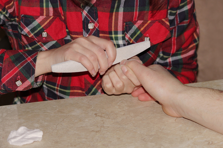 A student at the training courses of a manicure gives shape to nails the hand of a man client with a saw of a buffの写真素材