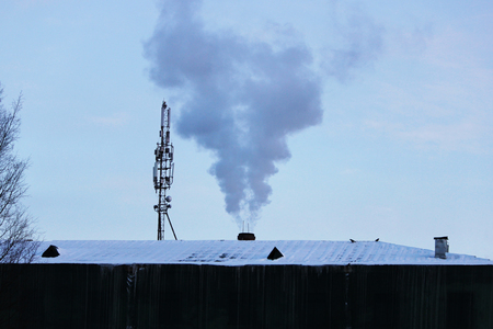 smoke from an industrial pipe and tower with antennas on a frosty winter dayの写真素材