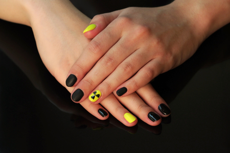 beautiful black-and-yellow manicure with shellac varnish in the form of a sign of radioactive danger. hands of the girl on a black shiny backgroundの写真素材