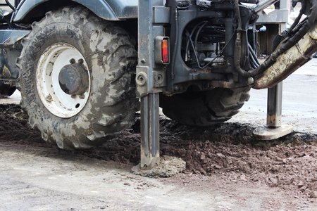 Tractor strong outrigger stabilizing legs extended to stabilize and steady state when digging the soil before applying an asphalt patch on a part of the road during repair.の写真素材