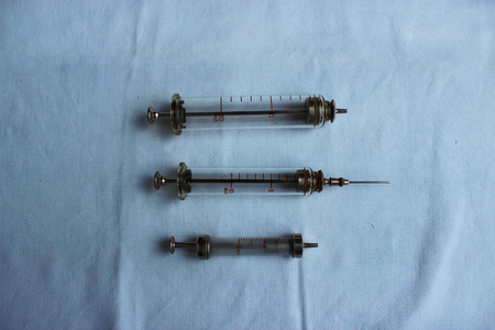 three old medical glass syringes lie on a blue clothの写真素材