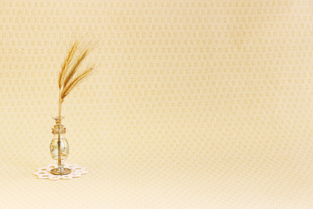 glass vase with a few ripe spikelets of rye Secale cereale on a white round knitted napkin on a beige backgroundの写真素材