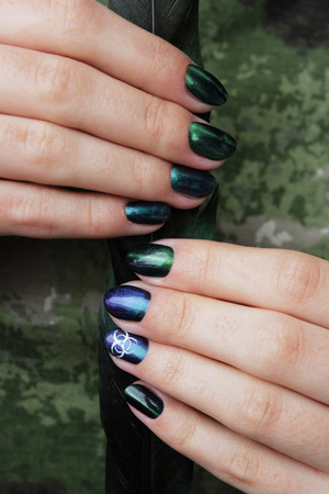 hands of a young girl with green manicure, which shows a sign of biological danger biohazard and black magpie feather. verticalの写真素材