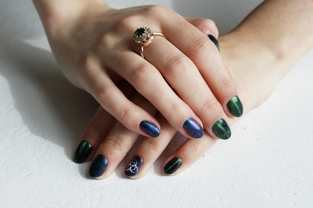 hands of a young girl with green manicure, which shows a sign of biological danger biohazard. On one finger - a gold ring with an emeraldの写真素材