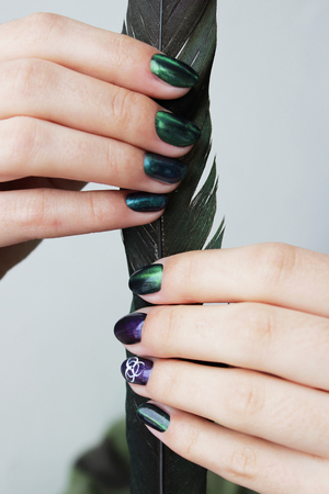 hands of a young girl with green manicure, which shows a sign of biological danger biohazard and black magpie feather. verticalの写真素材