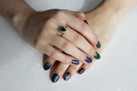 hands of a young girl with green manicure, which shows a sign of biological danger biohazard. On one finger - a gold ring with an emeraldの写真素材