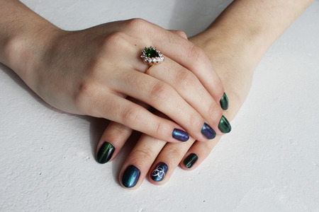 hands of a young girl with green manicure, which shows a sign of biological danger biohazard. On one finger - a gold ring with an emeraldの写真素材